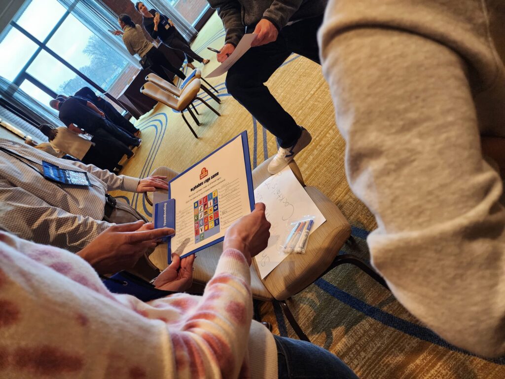 Team members collaborate on a trivia challenge during the Foodbank Showdown team building event, aiming to win coupons that will be exchanged for groceries to donate to a local charity.