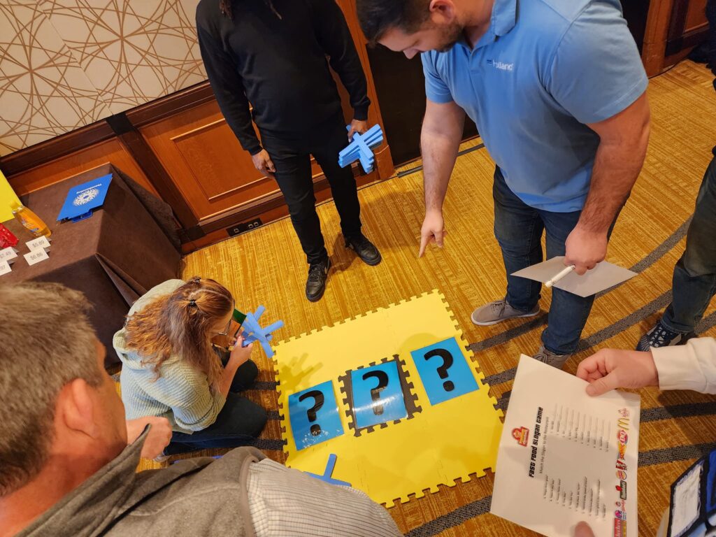 Team members gather around a puzzle challenge during the Foodbank Showdown team building event, strategizing to solve and earn Showdown Coupons for their grocery donations.