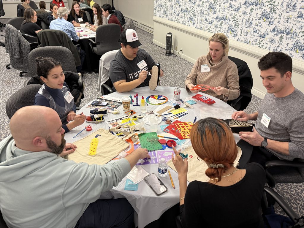 Teams creatively decorate TOMS shoes and tote bags during the Paint Soles for Souls team building event, using various paints and markers to design their unique artworks.