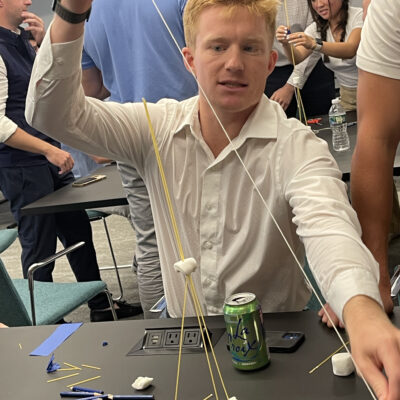 A participant at a corporate team building event working on a hands-on challenge, constructing a tower using spaghetti and marshmallows. The activity encourages problem-solving, creativity, and teamwork.