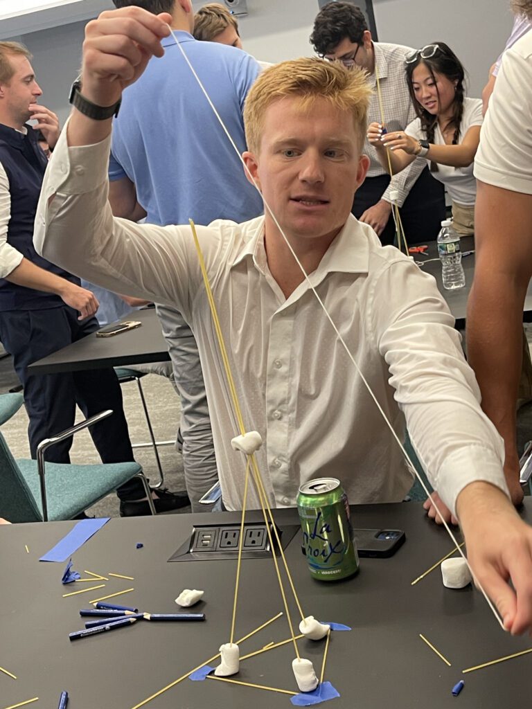 A participant at a corporate team building event working on a hands-on challenge, constructing a tower using spaghetti and marshmallows. The activity encourages problem-solving, creativity, and teamwork.