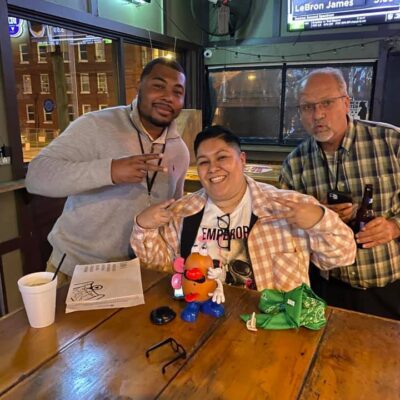 Team enjoying their Pub Crawl Scavenger Hunt, posing with playful props at a local bar, showcasing teamwork and camaraderie during the fun-filled event.