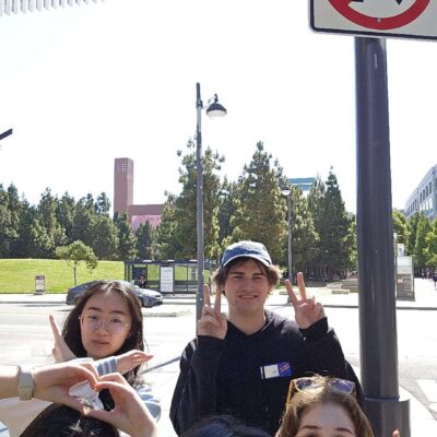 A group of five people smiling and making peace signs under a 'No U-turn' sign during a Team-opoly scavenger hunt.