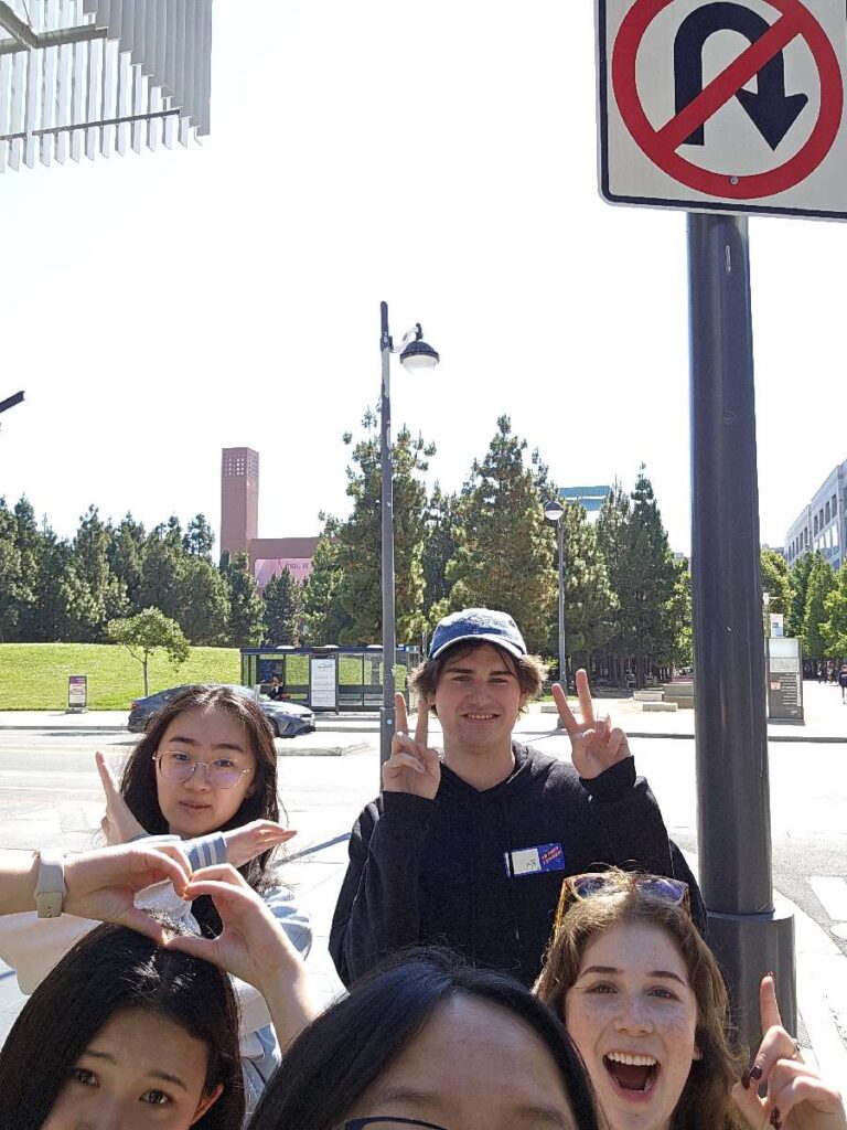 A group of five people smiling and making peace signs under a 'No U-turn' sign during a Team-opoly scavenger hunt.