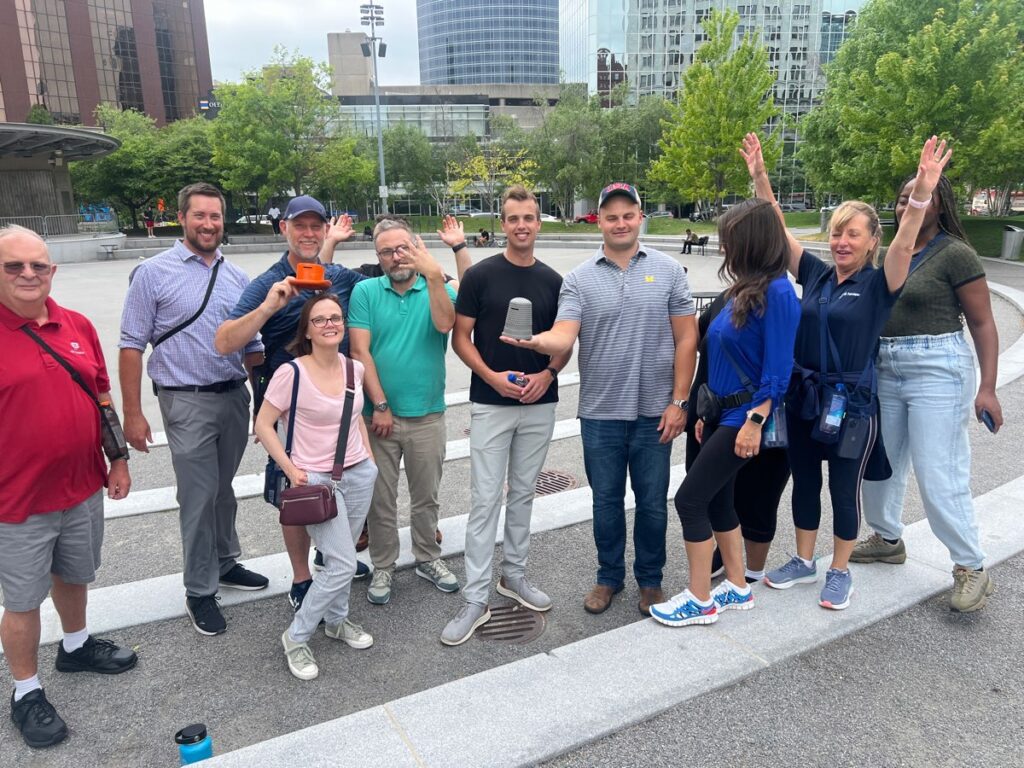 A team of participants smiling and posing in an outdoor plaza during a Team-opoly scavenger hunt team building event.