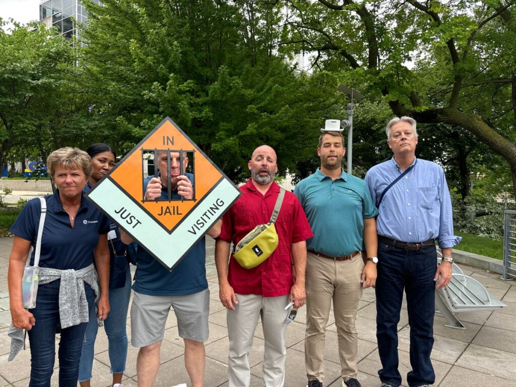 Team posing with a Monopoly-style 'In Jail' prop during a Team-opoly scavenger hunt team building event.