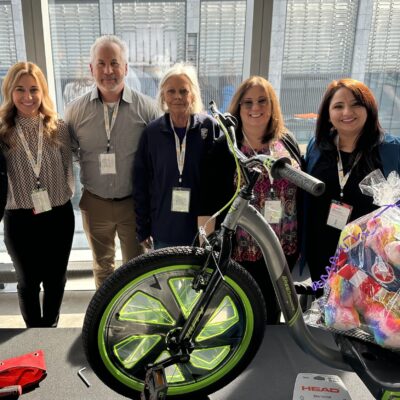 A group of five people standing behind a Green Machine bike with neon green wheels, proudly displaying their efforts for a charitable team building event.