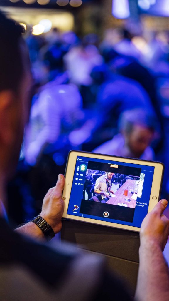 A participant engages with a tablet during a team building event, capturing moments of the activity in a lively, high-tech environment.