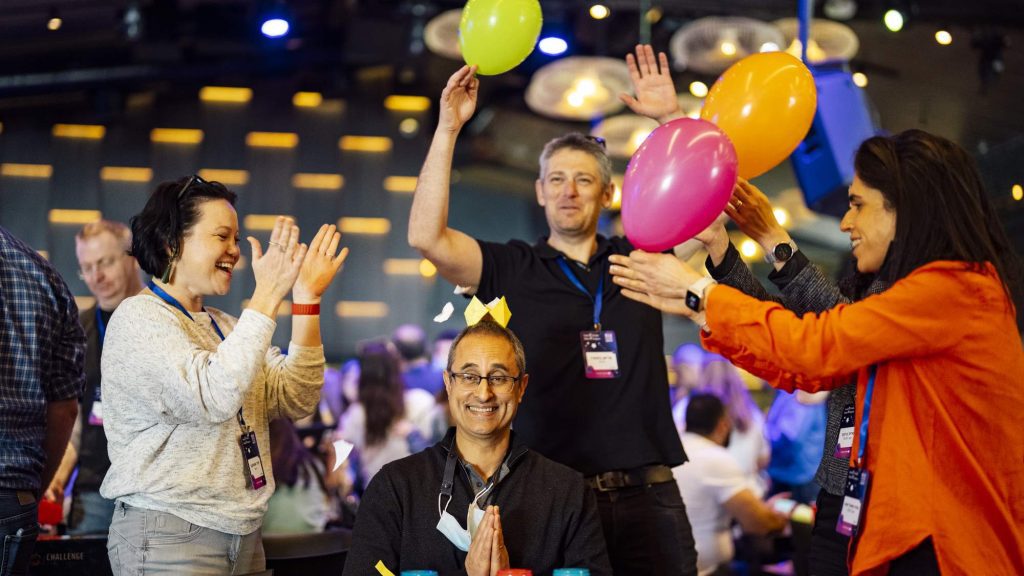 Participants are enthusiastically engaging with balloons as part of a creative challenge, working together to rack up points. The energy is high, and everyone is immersed in the fun, showcasing teamwork and leadership skills!