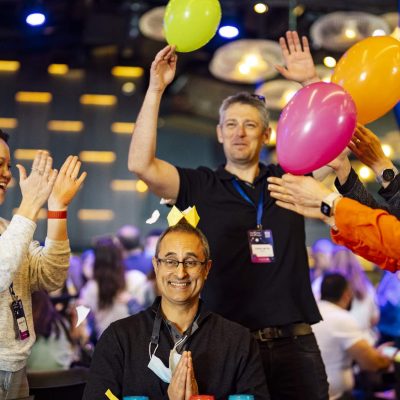 Participants are enthusiastically engaging with balloons as part of a creative challenge, working together to rack up points. The energy is high, and everyone is immersed in the fun, showcasing teamwork and leadership skills!