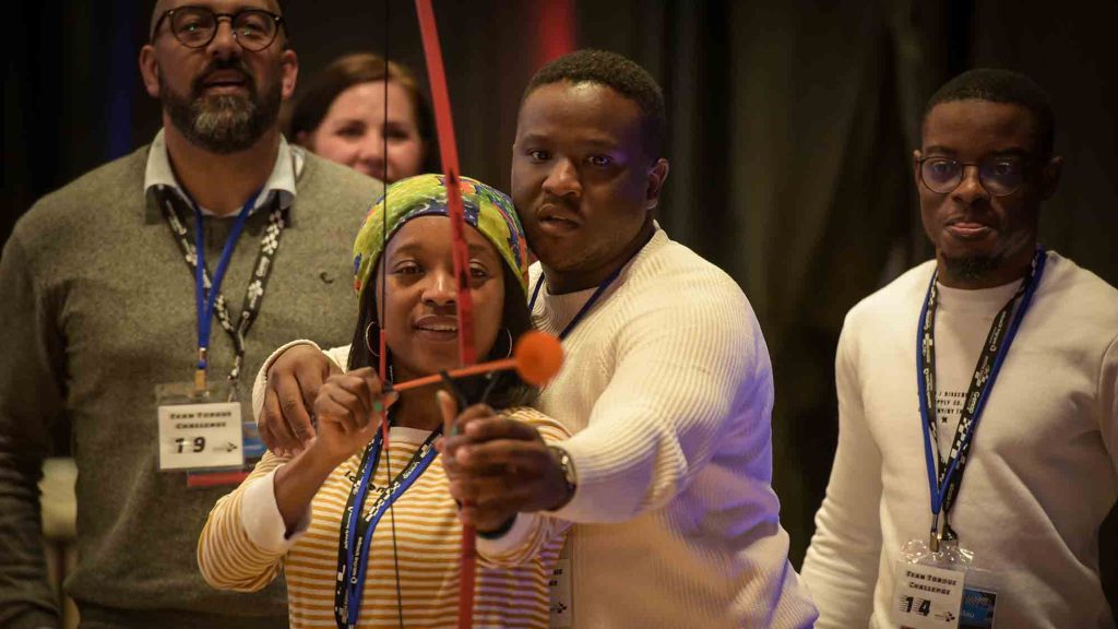 A group of participants focus intently while aiming a bow and arrow during a team building event, demonstrating their teamwork and precision.