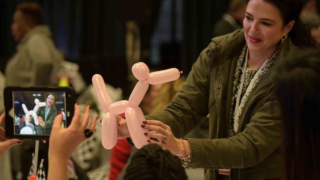 Participants engage in a fun and creative activity, forming a balloon dog while capturing the moment on their devices. This light-hearted task highlights teamwork, creativity, and a spirit of collaboration.