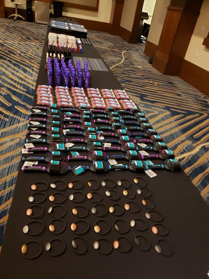 Tables lined with carefully arranged essential items, including brushes and personal care products, ready to be packed into handbags for donation during the Hopefull Handbags Global team building event.