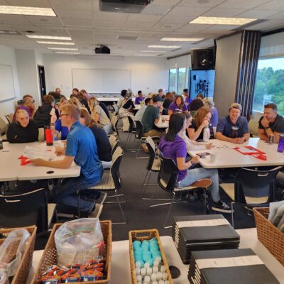 Teams gathered at a corporate team building session for Hopefull Handbags Global, preparing to pack essential items into handbags for women survivors of domestic abuse.