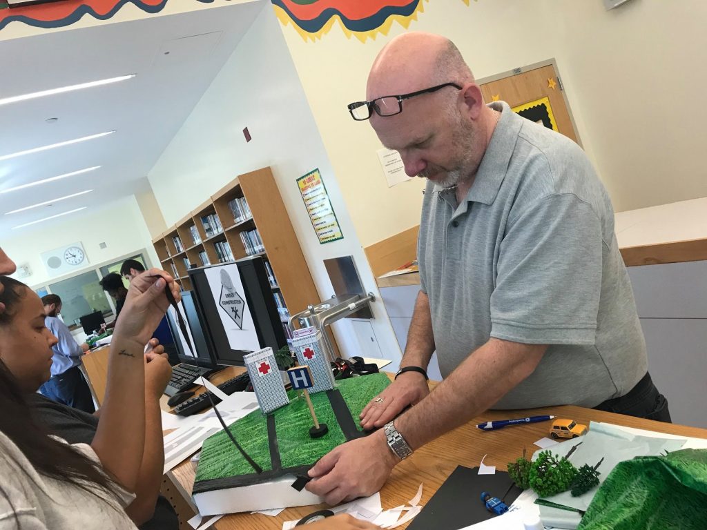 A participant carefully works on a miniature urban zone during a City Build team building event, focusing on adding details to the landscape.