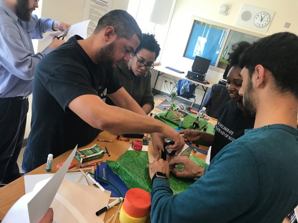 Team members collaborate on a City Build team building activity, constructing miniature urban landscapes using green materials and small props.