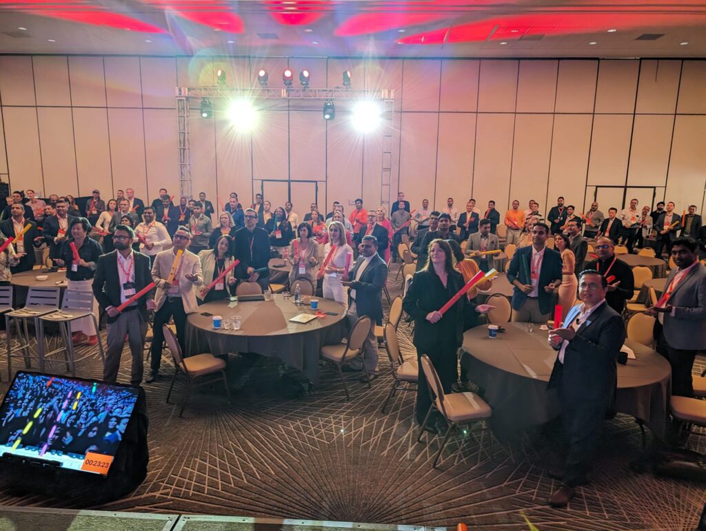 Conference attendees participating in a musical team building activity, holding colorful Boomwhackers and following along with rhythms on a large screen.