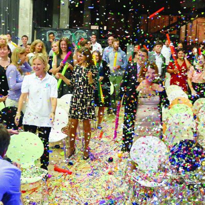 Team participating in Boom Time, a musical team building activity. Participants are surrounded by confetti and colorful Boomwhackers, collaborating to create music and enhance teamwork, energy, and communication.