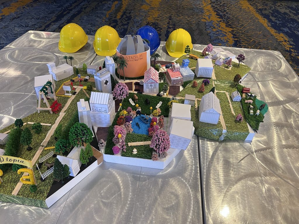 Close-up of a completed miniature city model at the City Build team building event, surrounded by yellow and blue hard hats, showcasing teamwork and creativity.