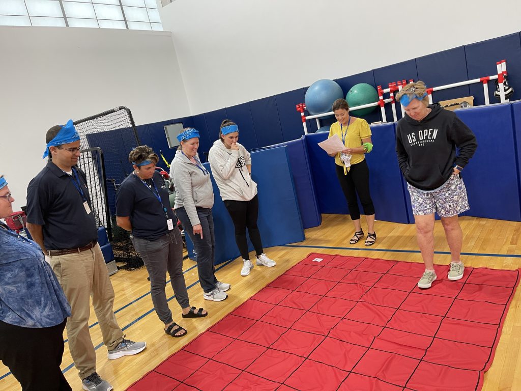 A group of participants in the Integrity team building event, working together while wearing blue headbands to complete a challenge on a large grid mat.