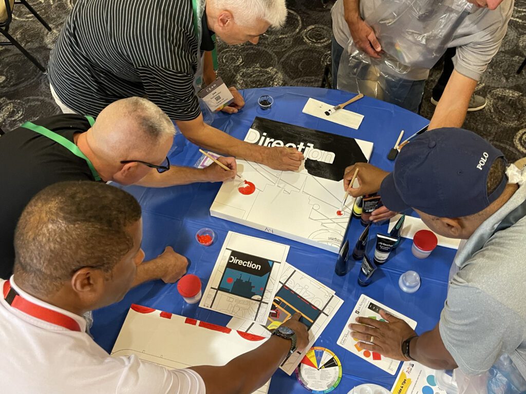 A group of participants works together painting sections of a mural during The Big Picture team building event, focusing on precision and collaboration to create a unified artwork.