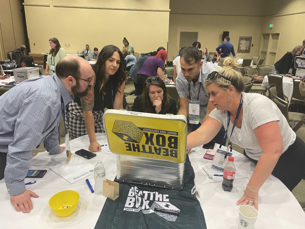 Team members gather around a challenge box during the Beat the Box team building event, strategizing together to solve escape room-style puzzles and unlock their way to victory.