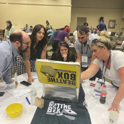 Team members gather around a challenge box during the Beat the Box team building event, strategizing together to solve escape room-style puzzles and unlock their way to victory.