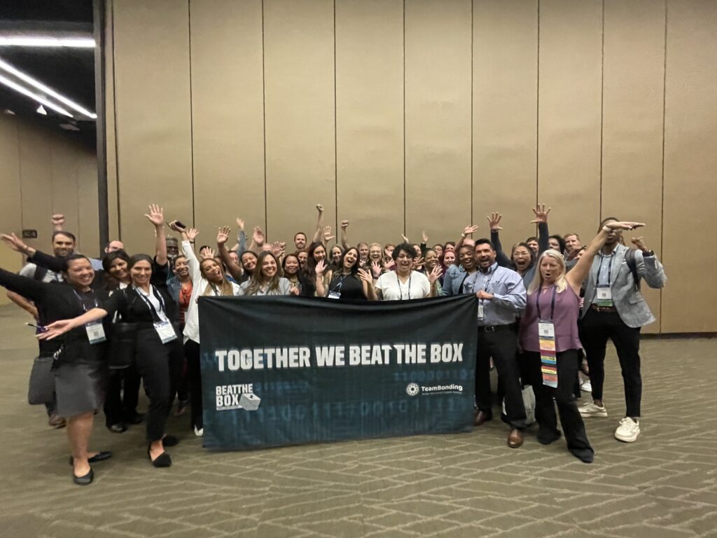 Large group of participants proudly displaying the 'Together We Beat The Box' banner after successfully completing a collaborative team building event.