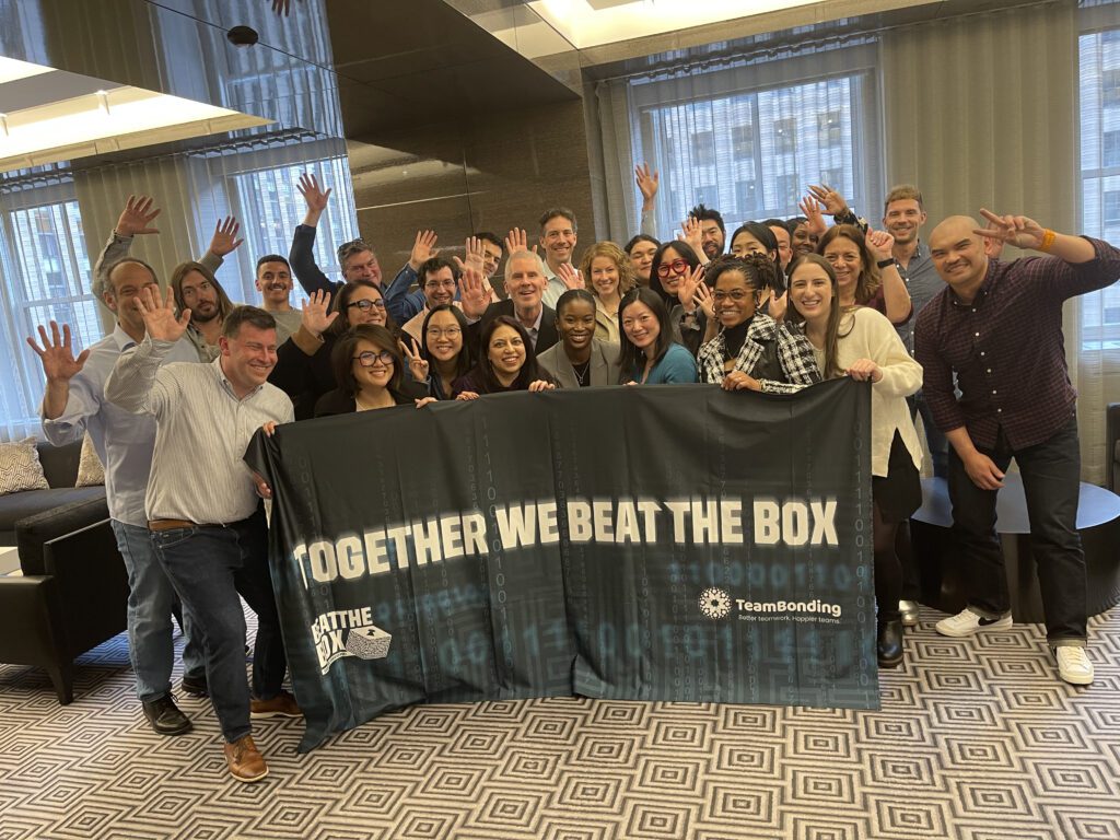 A large group of excited participants celebrate their victory after successfully completing the Beat The Box team building challenge, proudly displaying their teamwork banner.