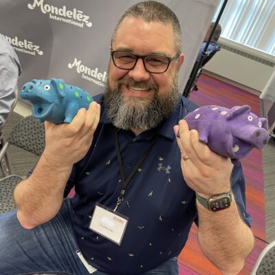 Man smiling and holding two colorful percussion instruments shaped like hippos during a BeatsWork team building activity.