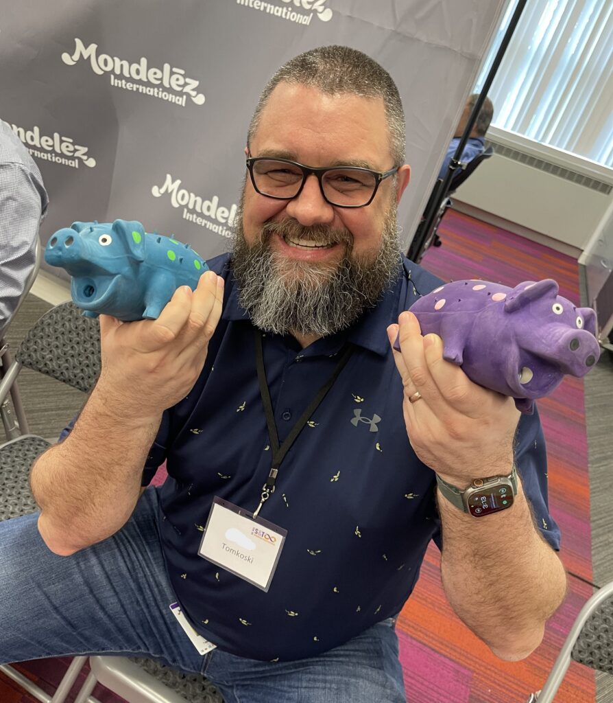 Man smiling and holding two colorful percussion instruments shaped like hippos during a BeatsWork team building activity.