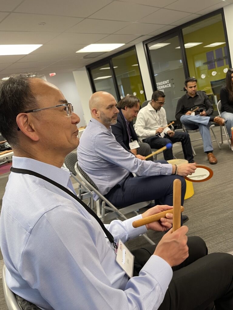 Participants seated in a circle during a BeatsWork team building event, each holding percussion instruments as they practice rhythms together. The group focuses on building rhythm and coordination as part of the drumming activity.