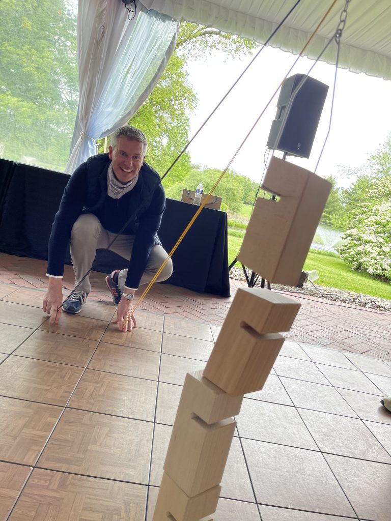 A participant smiling while carefully adjusting a stack of wooden blocks during the Integrity team building event, focusing on precision and collaboration.