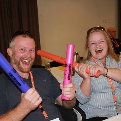 Team members smiling and laughing while participating in Boom Time, a musical team building activity. They use colorful Boomwhackers to create music, enhancing collaboration and boosting team spirit.