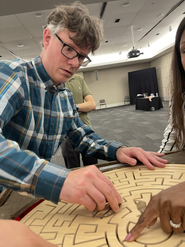 Participant concentrating on solving a wooden maze puzzle during the 'Escape The Maze' team building activity, enhancing problem-solving and teamwork skills.