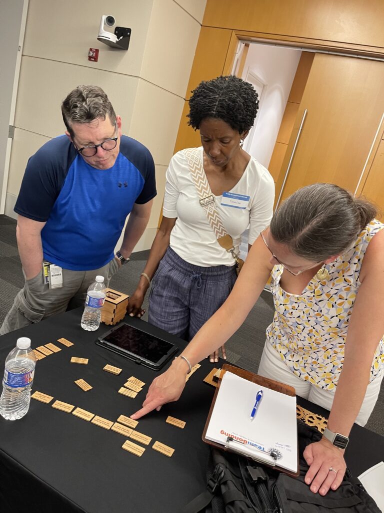 Three team members strategizing with wooden pieces during the 'Escape The Maze' team building event, focused on problem-solving and collaboration.