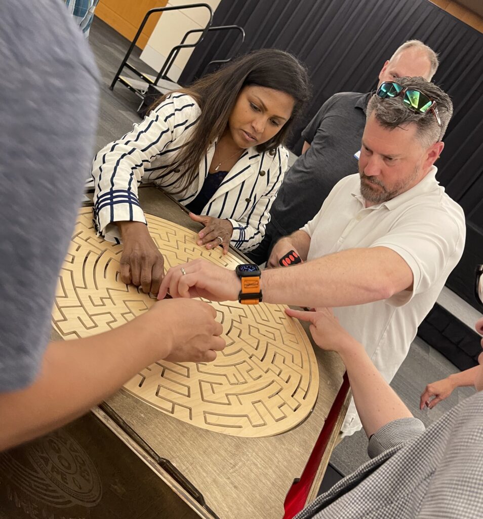 Participants focus on solving a wooden maze puzzle together during the 'Escape The Maze' team building activity, enhancing teamwork and problem-solving skills.