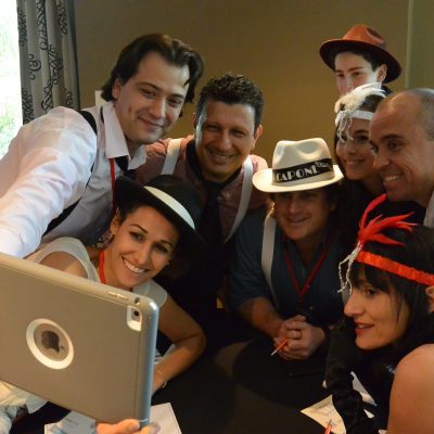 A team dressed in 1920s gangster-themed outfits gathers for a selfie during the high-energy Escape the Mob team building event, solving clues and creating their alibi.