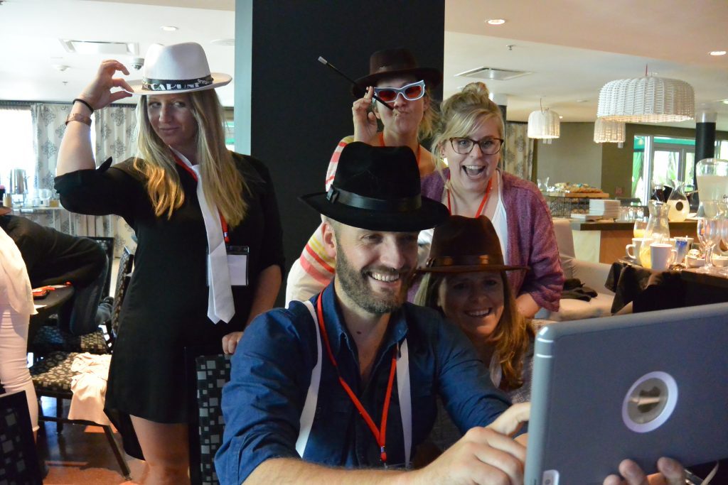 A team dressed in fun hats and posing for a photo during the Escape the Mob team building event, combining creativity and teamwork to solve the mystery.