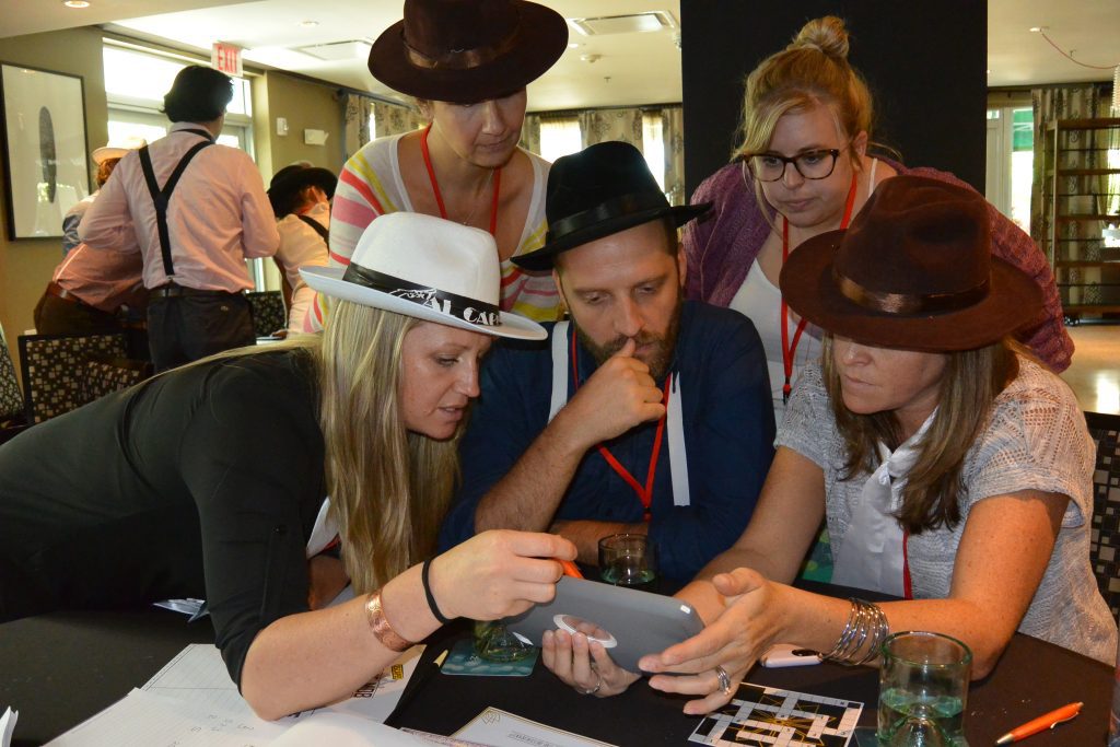 A focused team in the Escape the Mob team building challenge works together using an iPad to solve clues and establish their alibi in this high-energy mystery event.