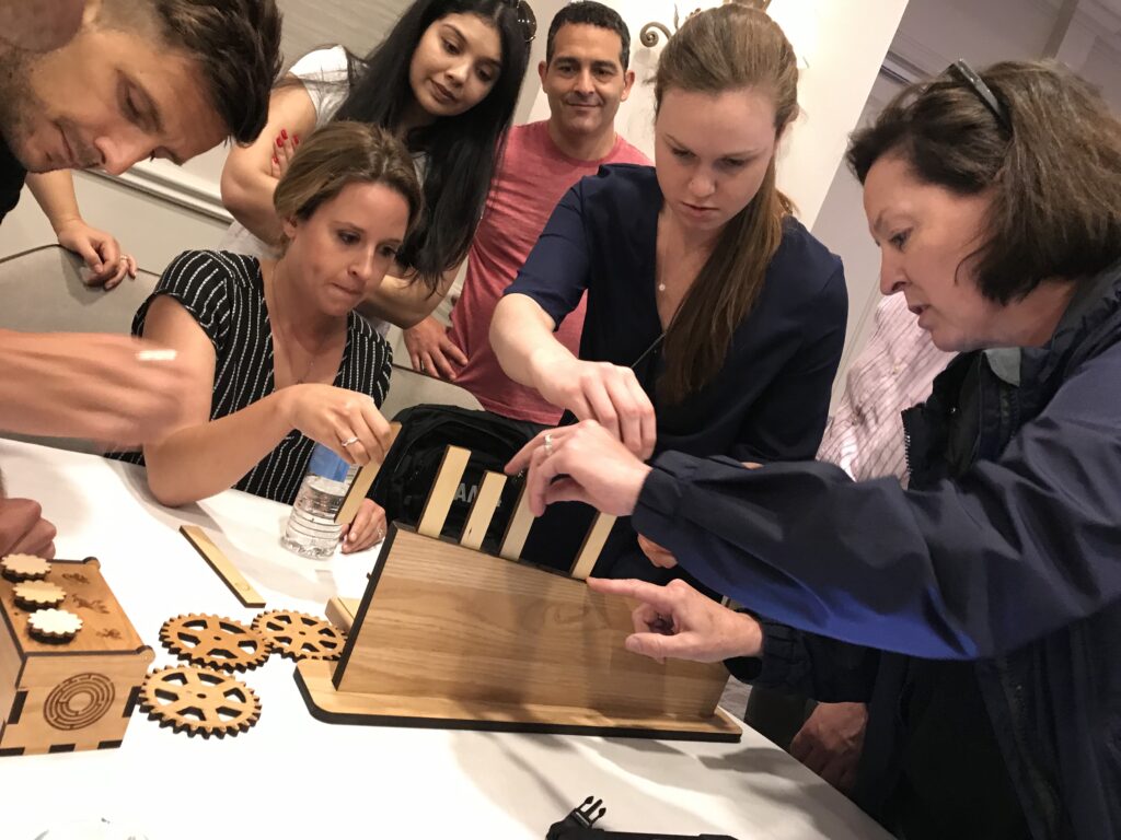 Focused participants work together to solve a puzzle box during the 'Escape The Maze' team building activity, demonstrating teamwork and problem-solving.