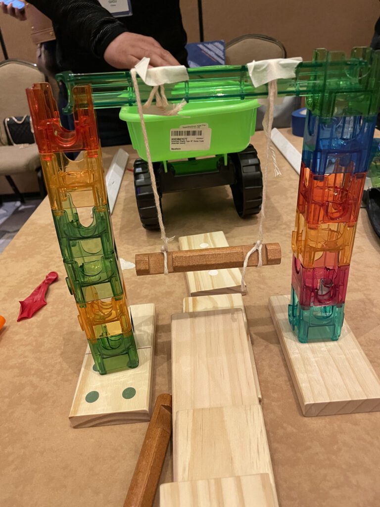 Colorful contraption setup for a chain reaction team building activity, featuring towers and a suspended bridge element crafted from various materials.