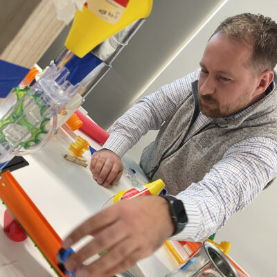 Participant working on a hands-on project during the Domino Effect team building event, focusing on creating Rube Goldberg-inspired contraptions to encourage creativity, problem-solving, and collaboration.