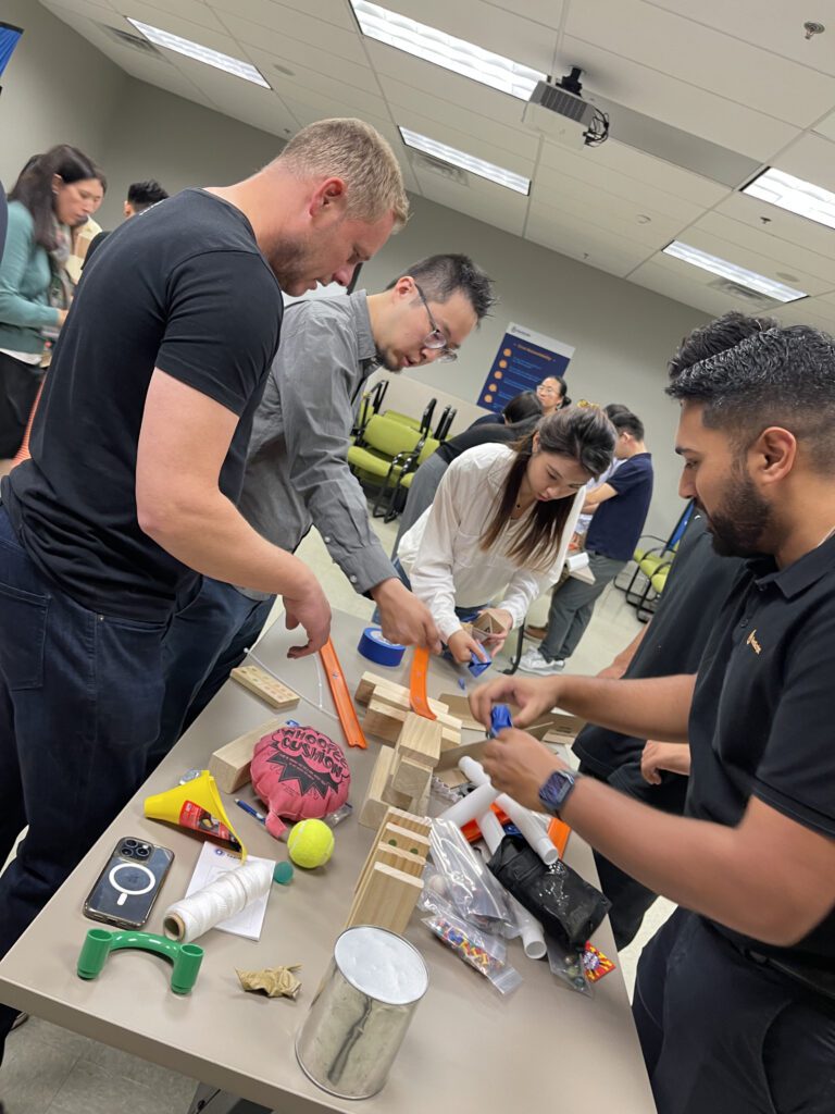 Group of participants collaboratively constructing a Rube Goldberg-style machine during the Domino Effect team building event.