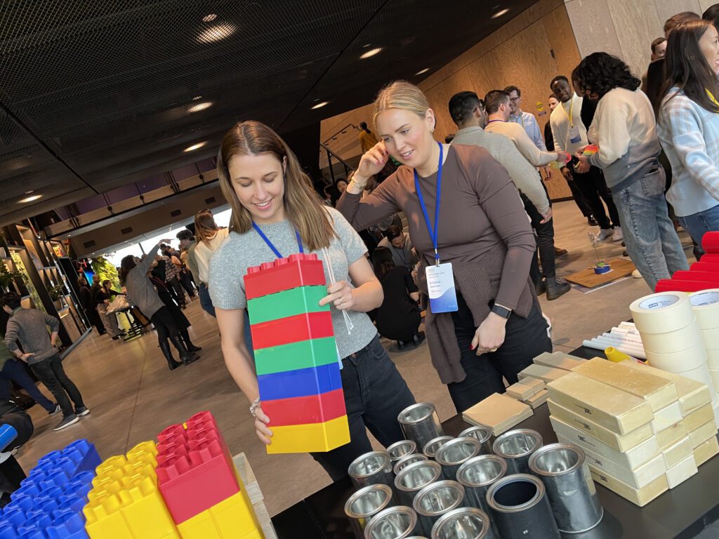 Team members work together during a chain reaction team building activity, assembling large colorful blocks as part of their Rube Goldberg-inspired machine.