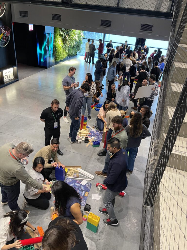 Teams collaborate in an open space to build complex, interconnected machines as part of a Chain Reaction team building event, fostering creativity and teamwork.