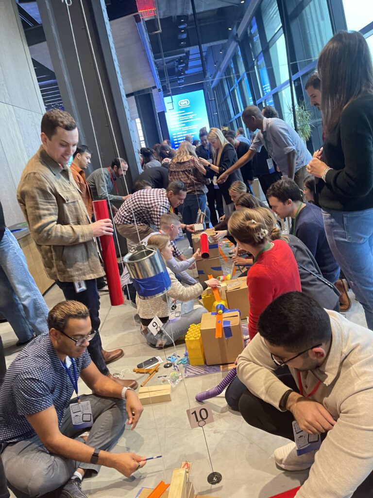 Participants collaborate on building intricate chain reaction machines on the floor during a dynamic team building event, enhancing teamwork and problem-solving skills.