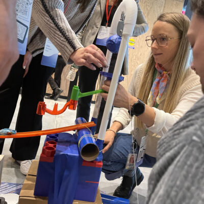 Participants carefully assemble pieces for a Rube Goldberg-inspired machine during a Chain Reaction team building activity, focusing on intricate connections and design.