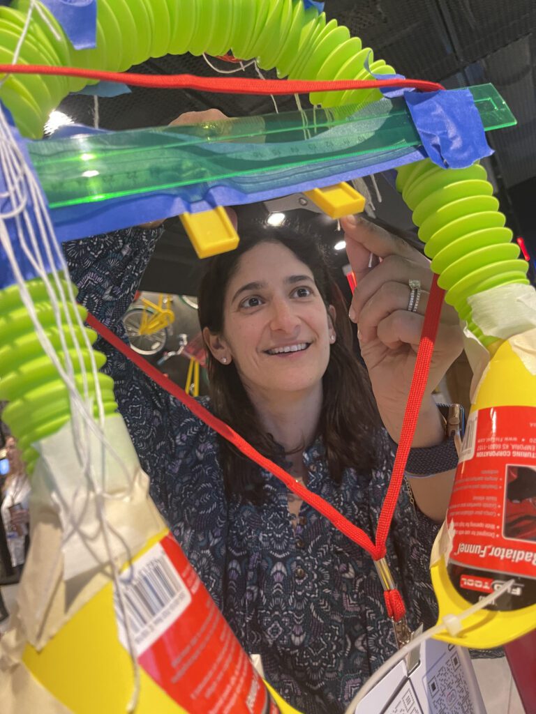 Participant carefully assembles a part of a complex Chain Reaction machine during a team building activity inspired by Rube Goldberg.