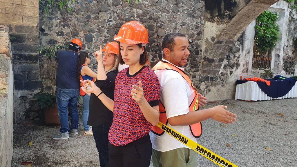 Outdoor team building activity focused on trust and communication. Paired participants wearing safety gear stand back-to-back, using non-verbal cues to complete the challenge, reinforcing teamwork and cooperation.